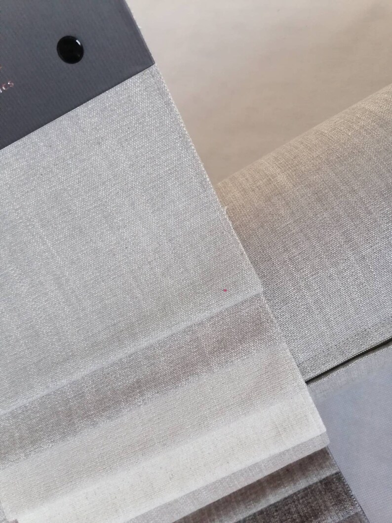 May include: Close-up of a fabric swatch book with different shades of gray linen fabric. The swatches are arranged in a stack, with the lightest shade on top and the darkest shade on the bottom.