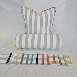 Può includere: Un set di cuscini e bolster a righe grigie e bianche con bordino rosso sul cuscino. Una selezione di cerniere in vari colori è esposta sotto i cuscini, tra cui nero, bianco, grigio, turchese, blu, navy, rosa, arancione, verde e giallo.
