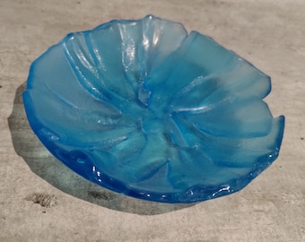 May include: A light blue glass dish with a flower-like design. The dish has a textured, frosted finish and a slightly wavy edge.