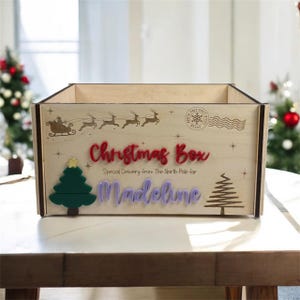 May include: Wooden Christmas box with the words "Christmas Box" in red, "Special Delivery from The North Pole for" and the name "Madeline" in purple. The box has a green Christmas tree and a gold star.
