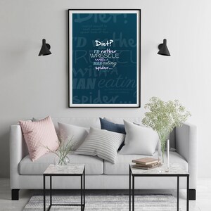 Puede incluir: Un póster azul verdoso con texto blanco que dice "¡Dieta!" y "Prefiero luchar con un hombre que come arañas..." El póster está enmarcado en negro y colgado en una pared blanca sobre un sofá gris con almohadas.