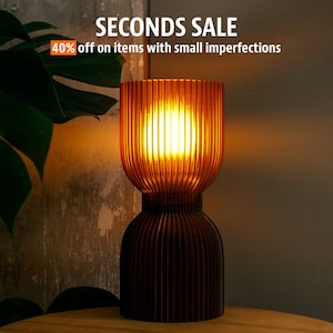 May include: A brown table lamp with a ribbed glass shade and a wooden base. The lamp is lit and casting a warm glow. The text "SECONDS SALE 40% off on items with small imperfections" is displayed above the lamp.