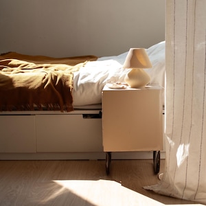 Unlit DUNE Table Lamp in beige 3D-printed recycled material, embodying 2025's Japandi and Organic Modern decor trends. Its nature-inspired dune texture graces a bedroom nightstand beside an ochre throw, promising soft ambient light for cozy, sustainable interiors. Perfect small (8.9"H) minimalist natural lamp.