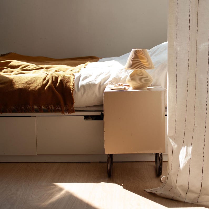 Unlit DUNE Table Lamp in beige 3D-printed recycled material, embodying 2025's Japandi and Organic Modern decor trends. Its nature-inspired dune texture graces a bedroom nightstand beside an ochre throw, promising soft ambient light for cozy, sustainable interiors. Perfect small (8.9"H) minimalist natural lamp.