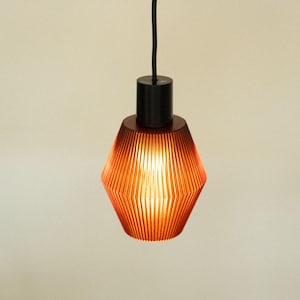 May include: A pendant light fixture featuring a translucent, ribbed, amber-colored shade with a geometric, faceted shape. The shade is attached to a solid black cylindrical socket cap and hangs from a black electrical cord, emitting a warm glow.