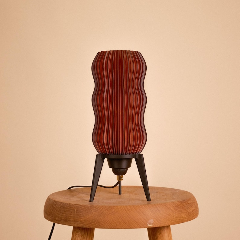 Wavy x Amber L table lamp product photo. Unique textured amber body made from recycled plastic sits on a retro tripod base. This eco-friendly lamp offers mid-century modern & space age style for warm ambient lighting (shown unlit).