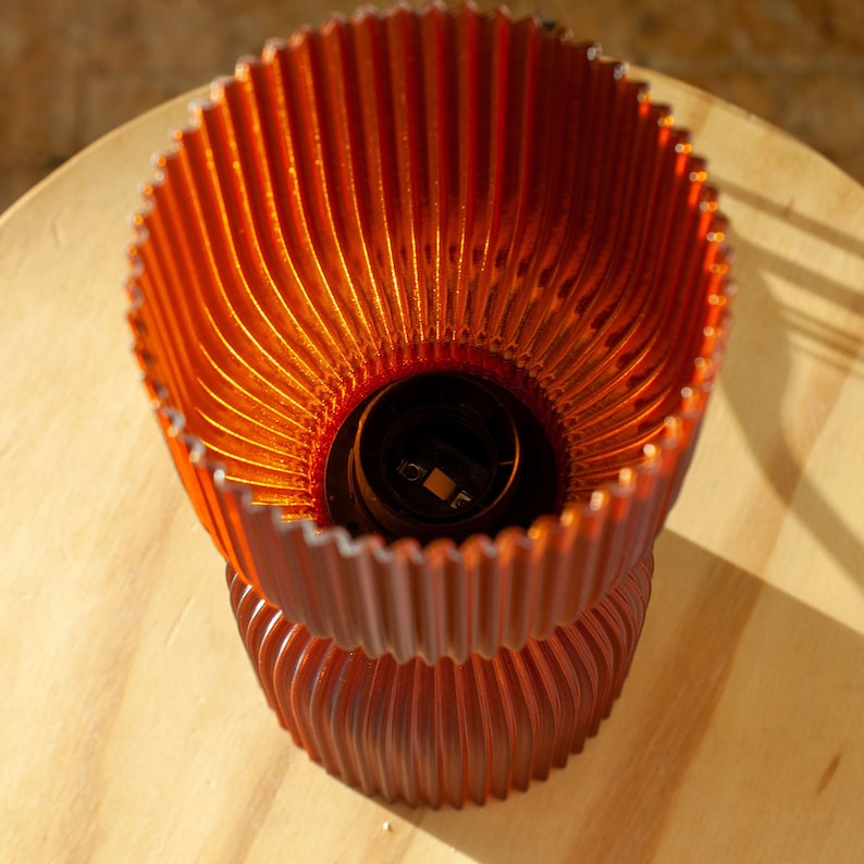 Top view of DIABOLO lamp showcasing sleek, curved silhouette. Sustainable lighting crafted from recycled plastic, offering warm amber glow. Enhances Scandinavian, modern, or minimalist interiors with eco-friendly, handcrafted charm.