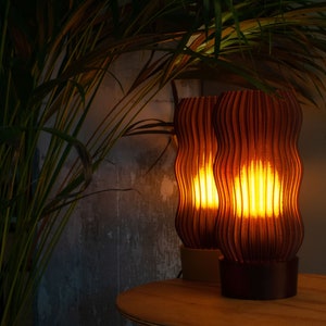 Warm amber glow from two elegant, wavy, ribbed table lamps made from eco-friendly recycled materials, placed beside lush green plants, perfect for cozy, modern, and sustainable home decor.