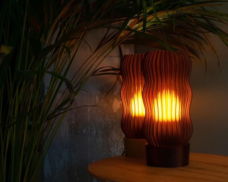 Warm amber glow from two elegant, wavy, ribbed table lamps made from eco-friendly recycled materials, placed beside lush green plants, perfect for cozy, modern, and sustainable home decor.