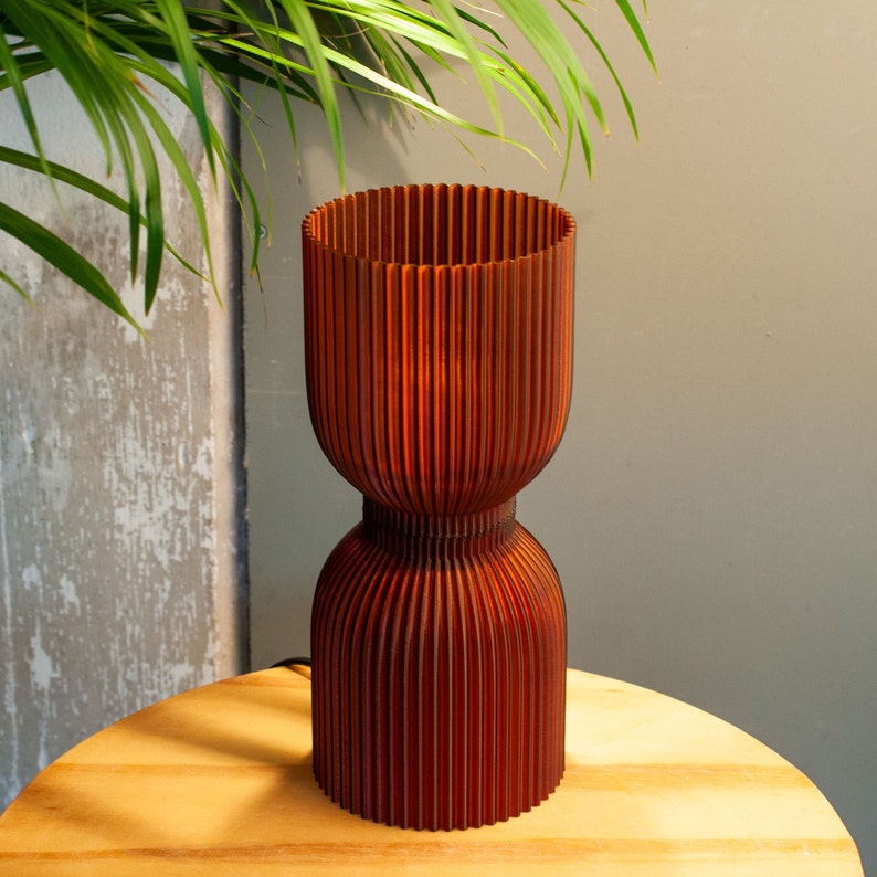 DIABOLO lamp styled on a wooden shelf with minimalist decor accents. Handcrafted from recycled plastic, adds a sustainable touch. Provides warm amber lighting perfect for cozy, modern, or boho home environments, enhancing ambiance.