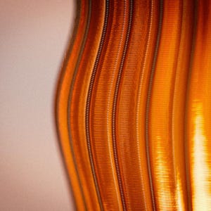 Peut inclure: Une vue rapproch&eacute;e d'une surface textur&eacute;e pr&eacute;sentant des cr&ecirc;tes verticales ondul&eacute;es dans des tons orange. Le motif se compose de lignes parall&egrave;les en relief qui cr&eacute;ent un effet rythm&eacute; et ondulant sur toute la surface, avec des reflets lumineux.