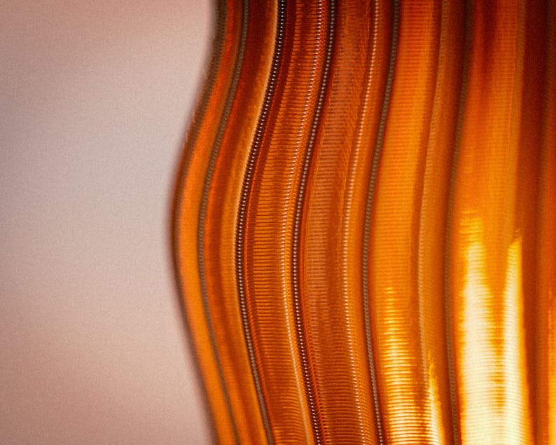 Peut inclure: Une vue rapproch&eacute;e d'une surface textur&eacute;e pr&eacute;sentant des cr&ecirc;tes verticales ondul&eacute;es dans des tons orange. Le motif se compose de lignes parall&egrave;les en relief qui cr&eacute;ent un effet rythm&eacute; et ondulant sur toute la surface, avec des reflets lumineux.