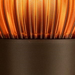 Peut inclure: Une vue rapproch&eacute;e d'une lampe avec un abat-jour en verre ambr&eacute; translucide dot&eacute; de textures nervur&eacute;es verticales. L'abat-jour repose sur une base cylindrique noire mate solide qui pr&eacute;sente de fines lignes horizontales sur sa surface.