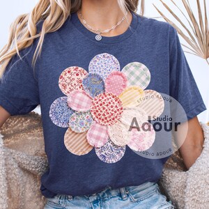 May include: A navy blue t-shirt with a large, colourful flower design. The flower is made of various fabric patches with floral, paisley, and gingham patterns. The text "Studio Adour" is printed on the shirt.