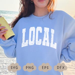 May include: A light blue sweatshirt with the word "LOCAL" in large, distressed white letters across the chest. The sweatshirt is a solid color, and the text has a vintage, worn look. The image also includes SVG, PNG, EPS, and DFX file type icons.