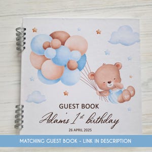 May include: A white guest book with a blue and brown watercolor illustration of a teddy bear holding balloons. The text "GUEST BOOK Adams 1st birthday 26 APRIL 2025" is printed on the cover.