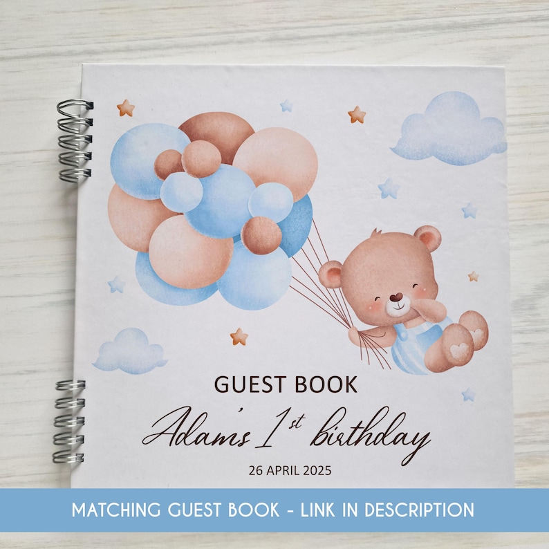 May include: A white guest book with a blue and brown watercolor illustration of a teddy bear holding balloons. The text "GUEST BOOK Adams 1st birthday 26 APRIL 2025" is printed on the cover.