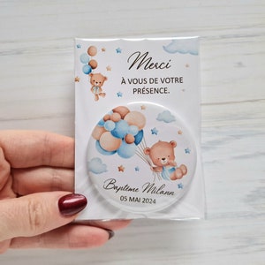 May include: A round mirror with a white background and a teddy bear holding blue and brown balloons. The mirror has the text "Baptime Milan 05 MAI 2024" and "Merci &agrave; vous de votre pr&eacute;sence."