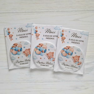 May include: Three round blue and brown favor buttons with a teddy bear holding balloons. The buttons have the text "Merci" and "A vous de votre presence" and "Bapteme Milann 05 MAI 2024".