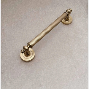 Op de afbeelding: Een goudkleurige deurklink in antieke stijl. De klink heeft een geribbeld, cilindrisch middengedeelte en decoratieve, afgeronde uiteinden. Hij is gemonteerd op ronde platen, wat een klassieke, elegante uitstraling creëert. De hardware is van metaal.