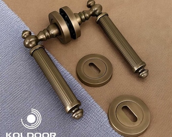 May include: Antique bronze door handle set with a keyhole cover. The handle has a ribbed design and a decorative end. The set includes two handles and two keyhole covers. The brand name "KOLDOOR" is visible in the bottom left corner.