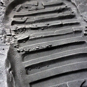 May include: A close-up of a footprint in the lunar dust. The footprint shows the distinct tread pattern of a boot.