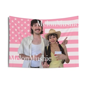 May include: A pink and white American flag tapestry with the text "MelonMushie" in white. The tapestry features a photo of two people. One person is wearing a straw hat and yellow top, and the other is wearing a white tank top.