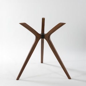May include: A wooden table base with a starburst design. The base has five legs that extend outwards from a central point, with a dark ring connecting the legs. The legs are made of a dark brown wood.