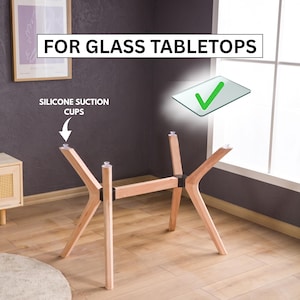 Op de afbeelding: Een lichtgekleurd houten tafelonderstel met vier schuine poten verbonden door een centrale balk. Op de bovenkant van elke poot zitten doorzichtige siliconen zuignappen. De tekst FOR GLASS TABLETOPS staat bij een groen vinkje afgebeeld.