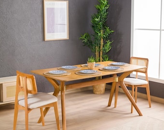 May include: A rectangular wooden dining table with four angled legs and two matching chairs featuring light-colored upholstered seats and woven cane backrests. The table is set with four round woven placemats and blue patterned plates.