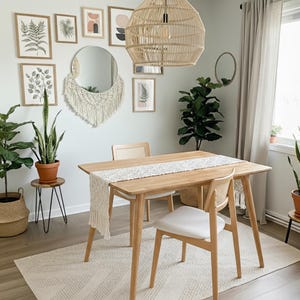 May include: A light wood dining table with two chairs, a woven pendant light, and a cream-colored rug. The room is decorated with framed botanical prints, a round mirror, and potted plants, creating a bright and airy dining space.