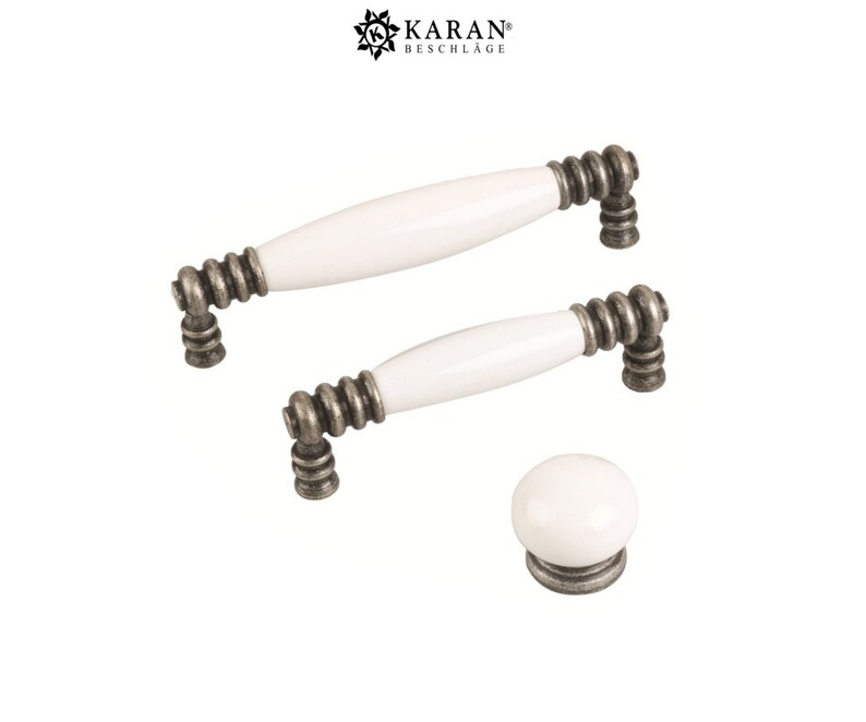 May include: Three white ceramic cabinet knobs with antique silver finish. The knobs are in different sizes, with two being long and one being round.