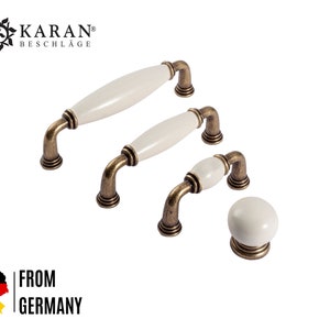 Può includere: Set di quattro pomelli per armadi in oro antico con dettagli in ceramica bianca. I pomelli sono di diverse dimensioni e forme, tra cui rotondi e ovali.