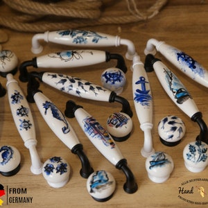 Pode incluir: Uma coleção de puxadores de gaveta de cerâmica branca com designs náuticos em azul e branco. Os puxadores são pintados à mão e apresentam vários designs, incluindo âncoras, cavalos-marinhos, navios e peixes. O texto "From Germany" e "Hand Made" é visível na imagem.