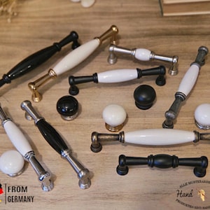 Könnte beinhalten: Sortiment an Keramik- und Metall-Schrankknöpfen und -griffen in Schwarz, Weiß und Gold. Die Knöpfe und Griffe werden auf einer Holzoberfläche präsentiert. "Hand Made" steht auf einem Etikett in der unteren rechten Ecke des Bildes.