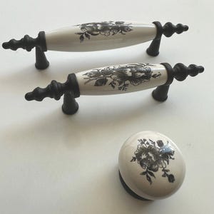 Può includere: Tre tiretti per cassetti in ceramica con disegni floreali neri e basi in metallo nero. I tiretti sono a forma di ovale lungo e pomo rotondo.