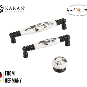 May include: Set of three black and white ceramic cabinet knobs with floral designs. The knobs are made by KARAN Beschl&auml;ge and are hand-made. The text "Hand Made" is visible in the image.