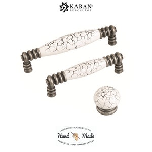 May include: Three white ceramic cabinet knobs with a crackled finish and silver metal accents. The knobs are in the shape of a cylinder and a sphere. The text "Hand Made" is visible in the image.
