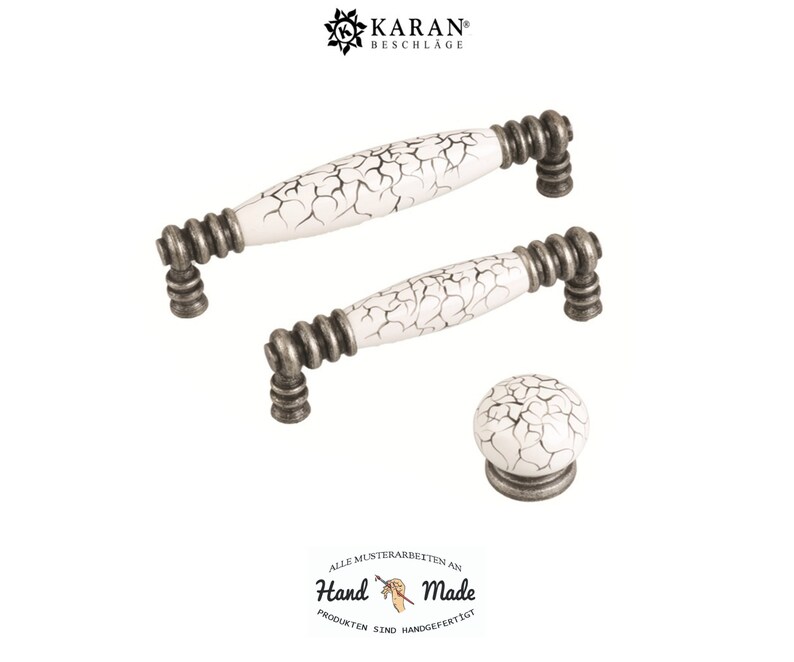 May include: Three white ceramic cabinet knobs with a crackled finish and silver metal accents. The knobs are in the shape of a cylinder and a sphere. The text "Hand Made" is visible in the image.