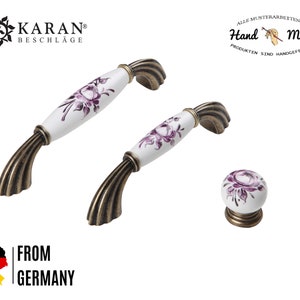 May include: Two white ceramic cabinet knobs with purple floral designs and antique brass bases. A single knob is also shown. All items are hand-made.