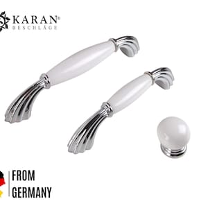 Könnte beinhalten: Zwei weiße Keramik-Schrankknöpfe mit Chromoberfläche und dekorativem Design. Die Knöpfe haben einen Durchmesser von 3,8 cm.