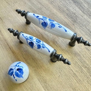 May include: Three ceramic drawer pulls with a blue and white floral design. The pulls have a silver finish and are shaped like a long oval.