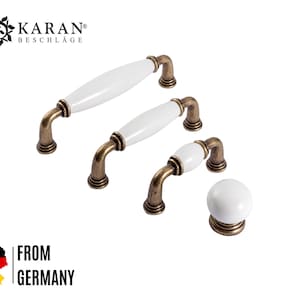 Könnte beinhalten: Satz von vier weißen Keramik-Schrankknöpfen mit antiken Messingakzenten. Die Knöpfe sind in verschiedenen Größen und Formen, einschließlich rund und oval.