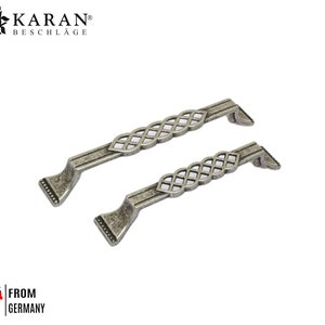 May include: Two silver-toned cabinet door pulls with a decorative, woven design. The pulls are approximately 12 cm long.