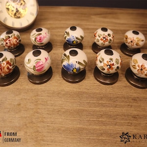 Peut inclure: Dix boutons de porte en céramique avec des motifs floraux dans des tons de rose, bleu, orange et vert. Les boutons sont blancs avec une base dorée.