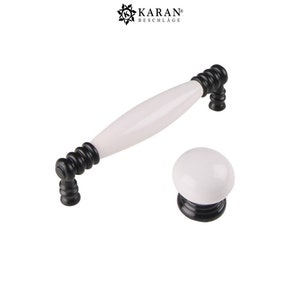 May include: White ceramic cabinet knob and pull with black accents. The pull is a long, oval shape with a rounded end. The knob is round.