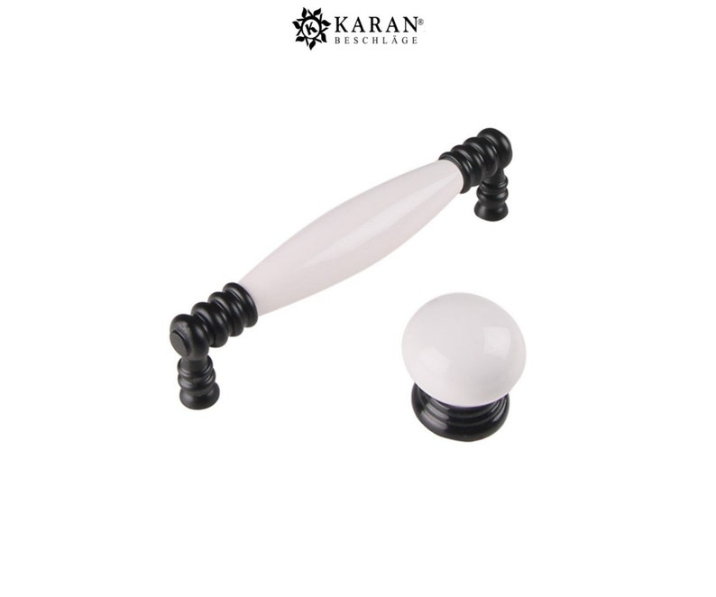 May include: White ceramic cabinet knob and pull with black accents. The pull is a long, oval shape with a rounded end. The knob is round.