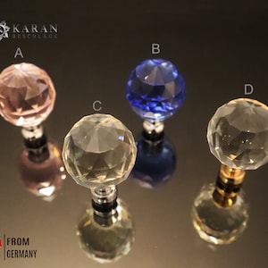 Könnte beinhalten: Vier Kristall-Schrankknöpfe in verschiedenen Farben: rosa, blau, klar und klar mit goldener Basis. Die Knöpfe sind rund und haben ein facettierten Design. Der Text "KARAN BESCHLAGE" ist in der oberen linken Ecke des Bildes sichtbar.