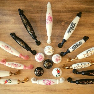 Könnte beinhalten: Sortiment an Keramik-Schrankknöpfen mit floralen und geometrischen Designs in Schwarz, Weiß und Rosa. Die Knöpfe sind kreisförmig auf einer Holzoberfläche angeordnet.  FROM GERMANY.