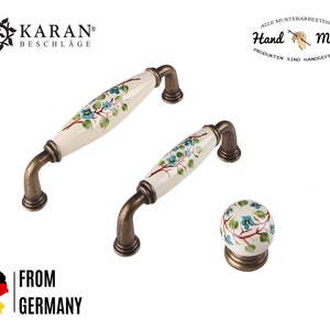 Könnte beinhalten: Zwei weiße Keramik-Schrankknöpfe mit Blumenmuster und antikem Messingbeschlag. Die Knöpfe haben einen Durchmesser von 3,8 cm und eine Länge von 7,6 cm. Der kleinere Knopf ist ein runder Knopf mit Blumenmuster. Alle Musterarbeiten sind handgefertigt. Die Produkte sind handgefertigt.